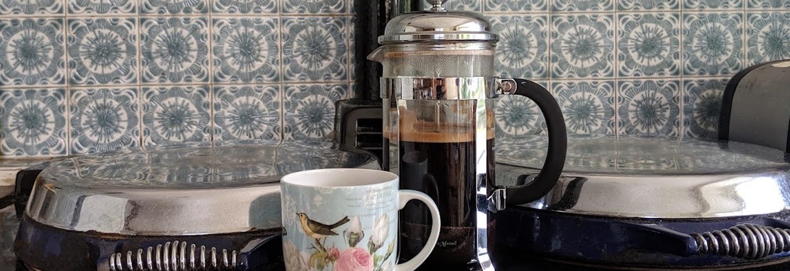 A French press of fresh coffee and a floral mug on the stovetop
